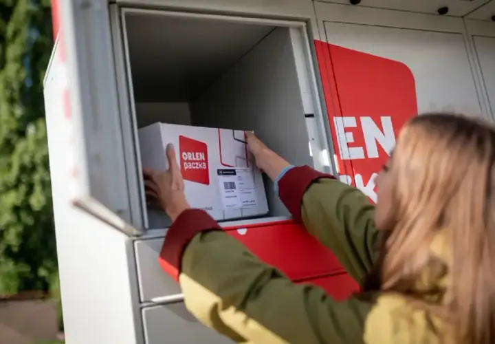 Kobieta wkłada paczkę z logo "Orlen paczka" do skrytki automatu paczkowego.